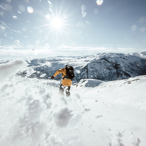 Action shot of a person in a yellow jacket snowboarding down a mountain