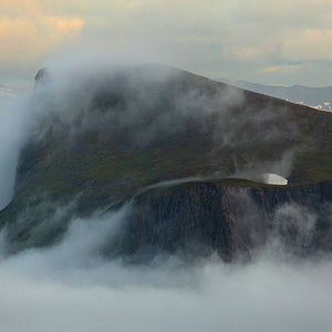 Photo of a green mountain top surrounded by mist