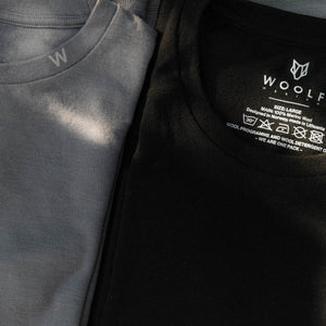 Image of two folded Woolf Merino tees, one black and one grey.