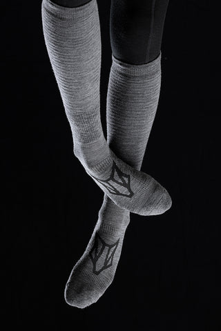 Image of a person's legs wearing the Torset Thin Sock in grey, against a black background