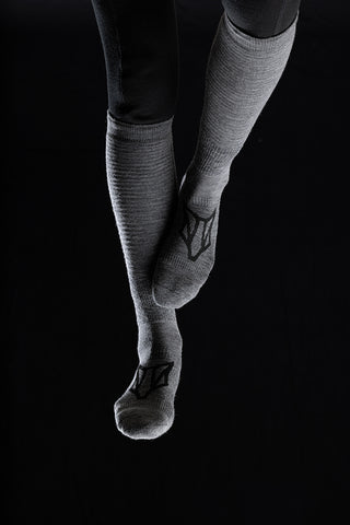 Image of a person's legs wearing the Torset Thin Sock in grey, against a black background