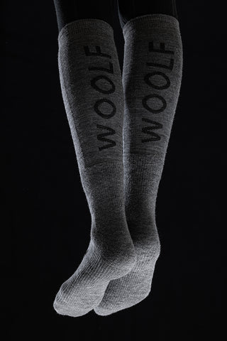 Image of a person's legs from the back wearing the Torset Thin Sock in grey, against a black background