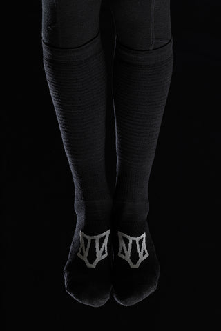 Image of a person's legs wearing the Torset Thin Sock in black, against a black background